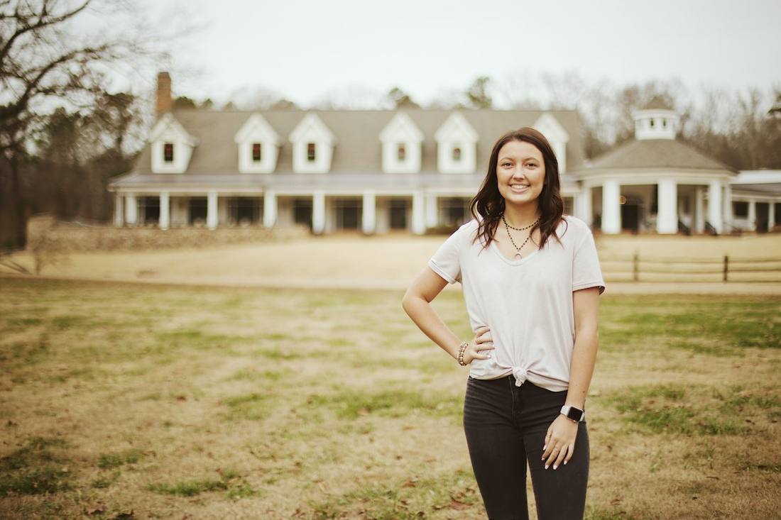 A woman standing in a field in front of a large white farmhouse