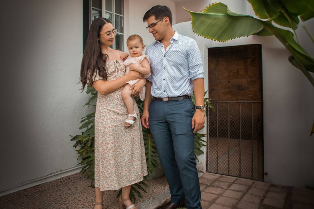 A young couple holding a baby outside their house
